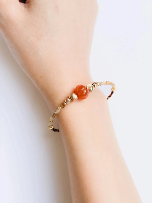 Japanese Minimalist Beaded Bracelet with Tiger Eye crystal, golden rutile crystal, orange, and gold elements with a red bead on a wrist against a white background