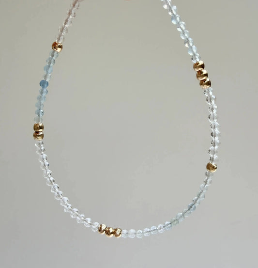 Japanese Minimalist Bracelet with blue aquamarine, clear crystal, and gold accents with a gray background