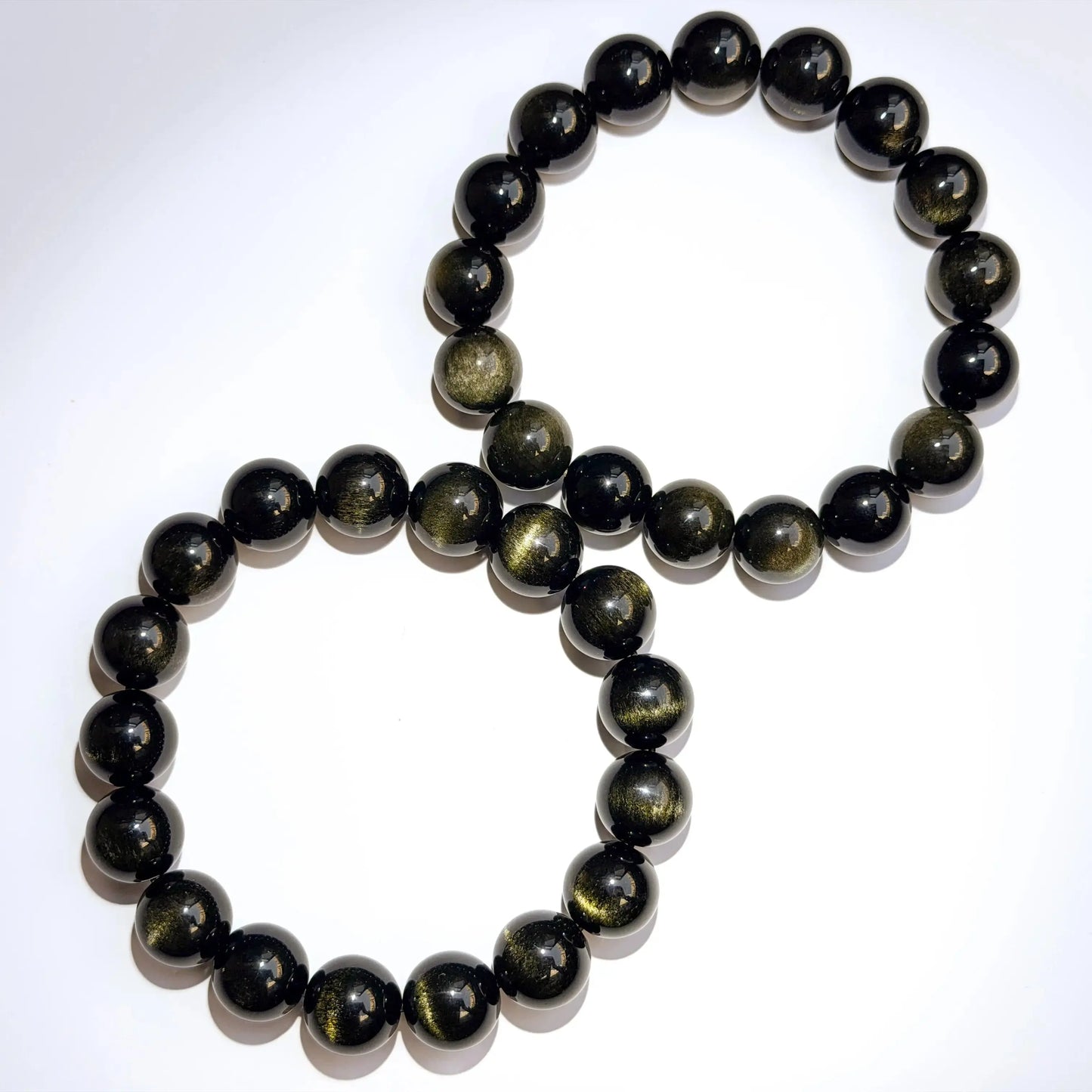 two gold sheen obsidian bracelets on white desk