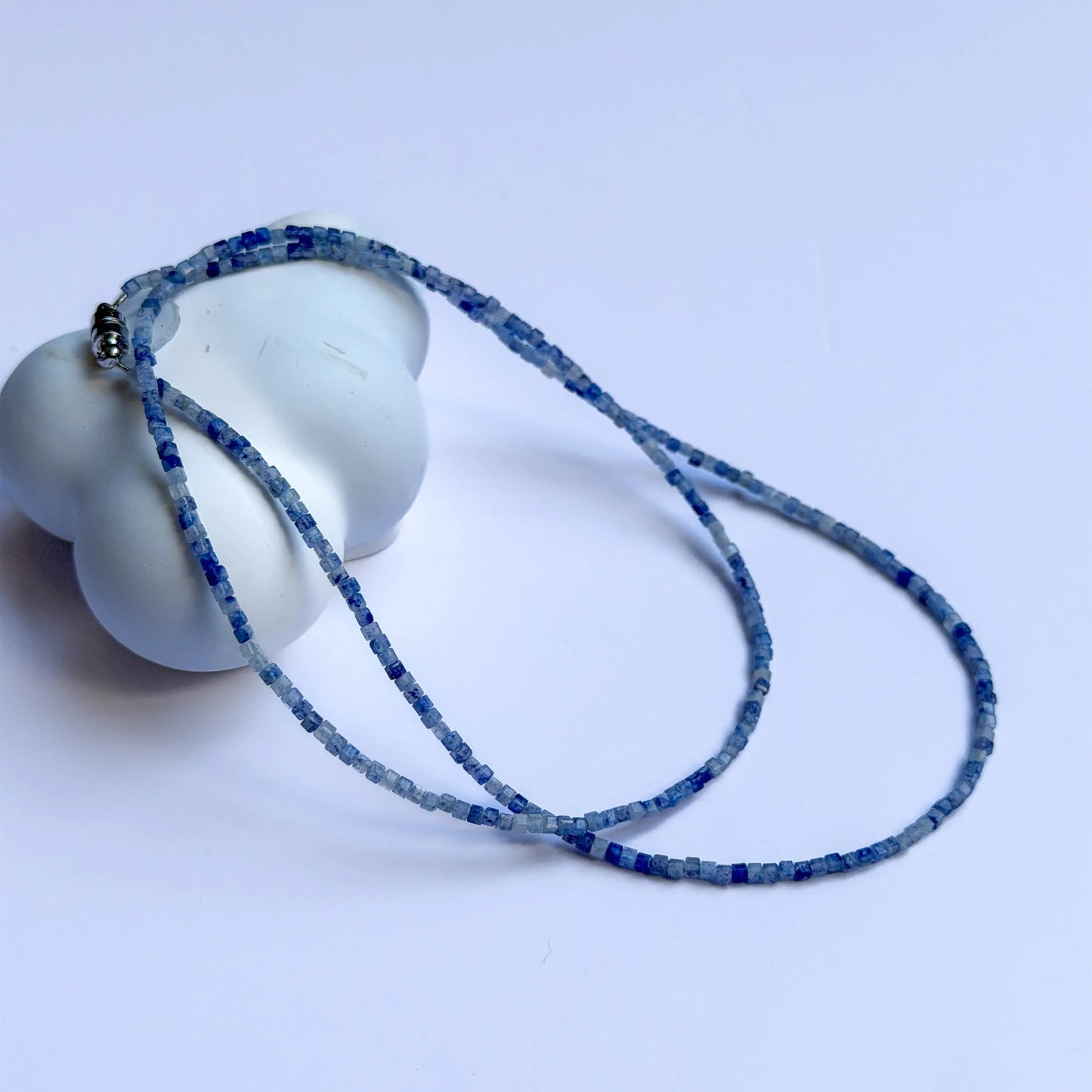 Blue sodalite crystal beaded necklace draped over a white ceramic object on a light blue background