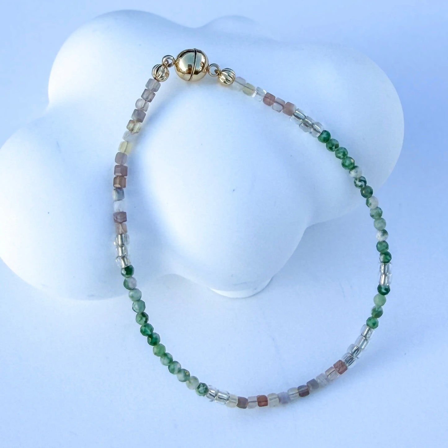Bracelet with green and white jade beads on a white mannequin bust against a light blue background