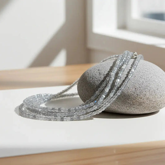 a grey beaded necklace displayed on a grey tumble stone