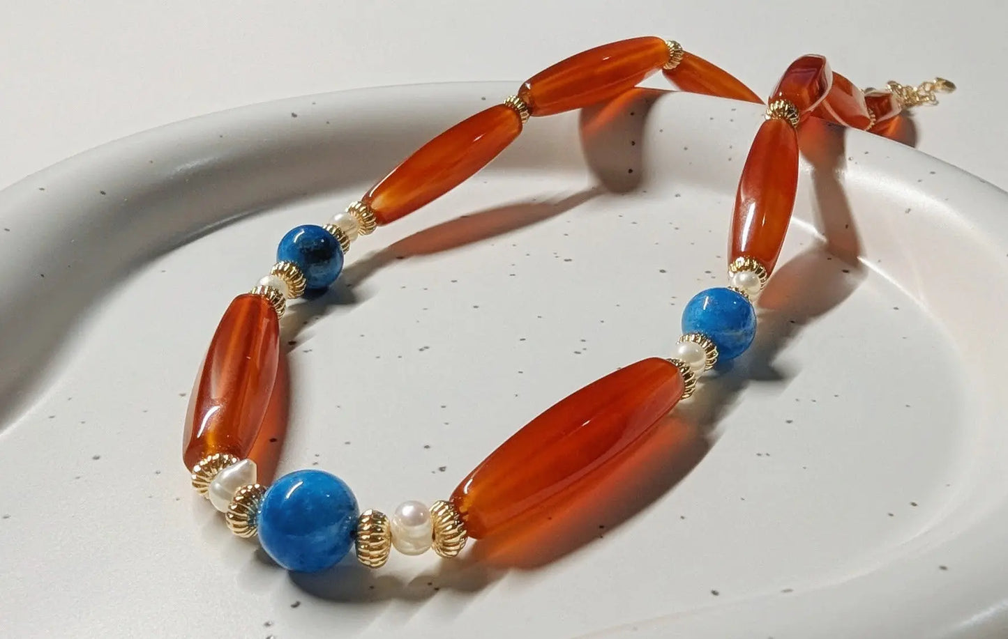 Necklace with orange, blue, and pearl beads on a white plate