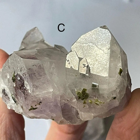 Clear crystal with green crystals held between fingers against a neutral background