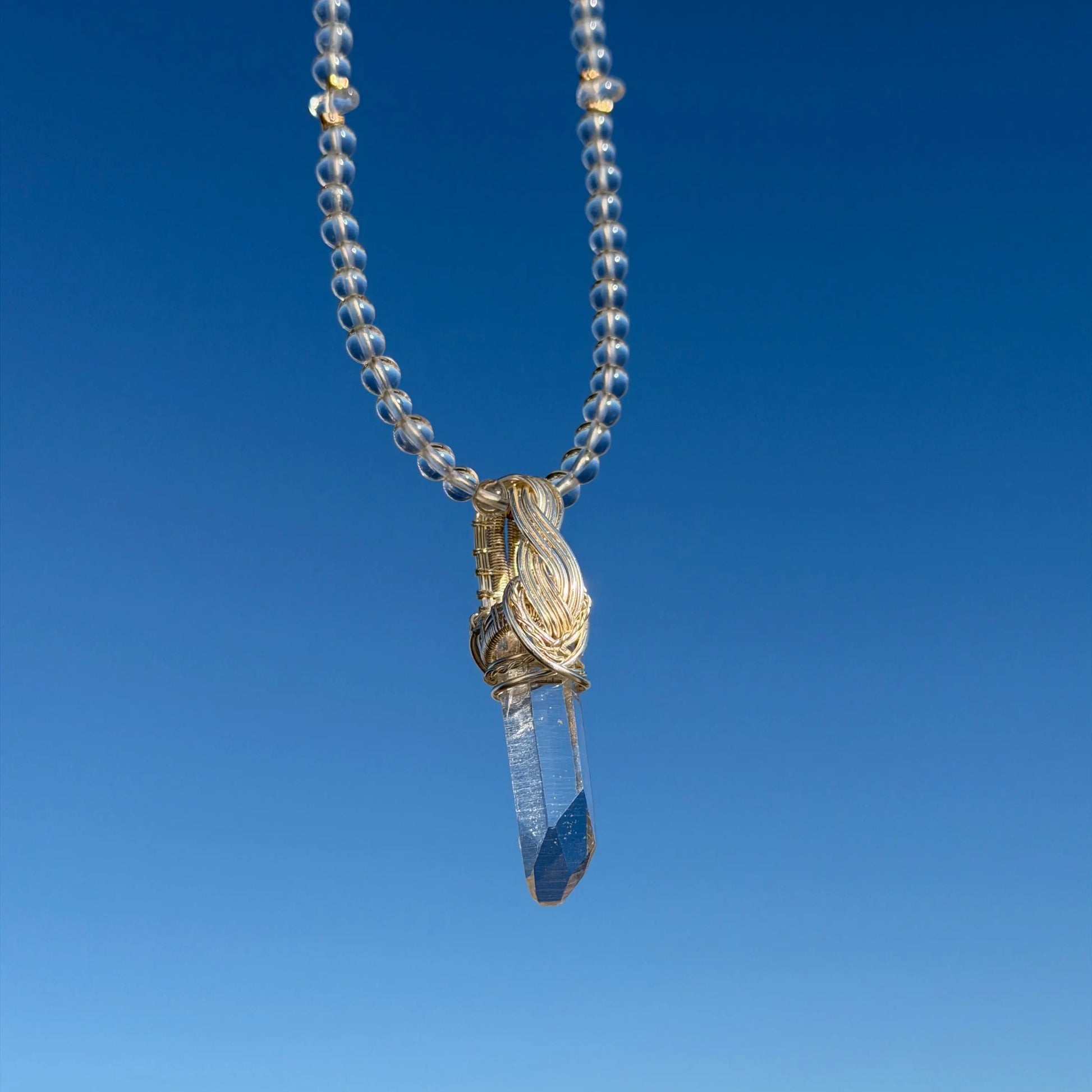 Necklace with a clear beaded chain and gold clasp against a blue sky background