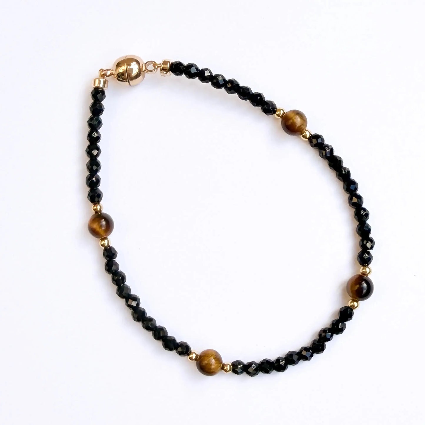 Black beaded bracelet with gold accents on a white stone surface