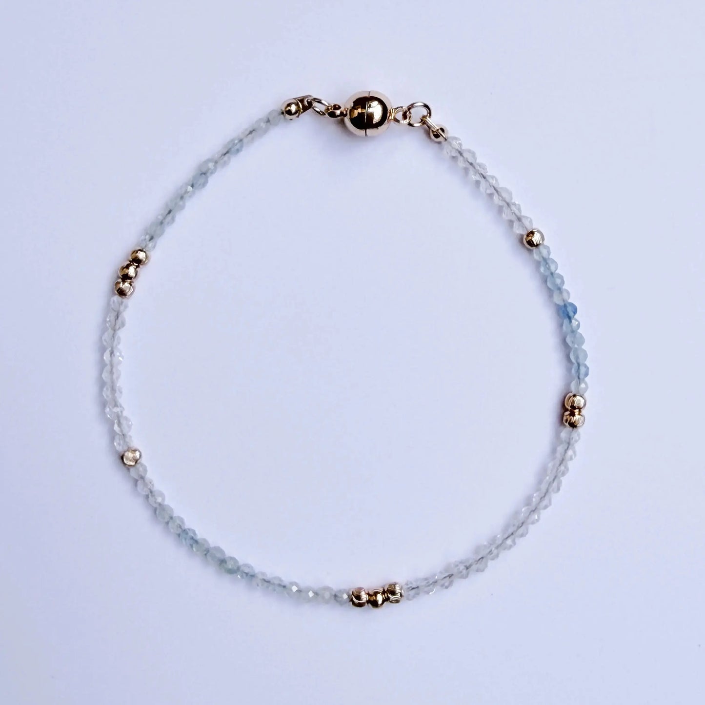 Japanese Minimalist Bracelet with blue aquamarine, clear crystal, and gold accents on a white surface