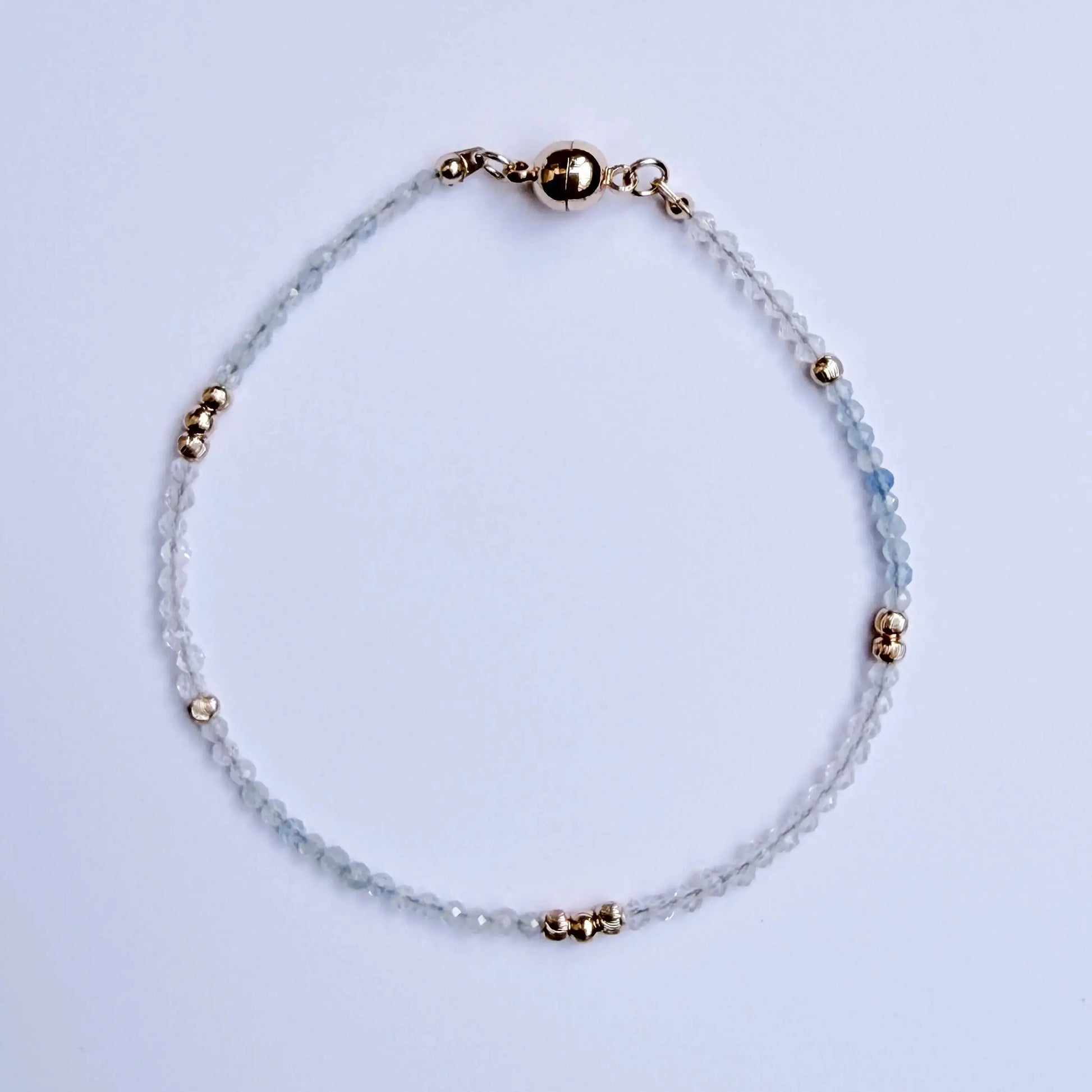 Japanese Minimalist Bracelet with blue aquamarine, clear crystal, and gold accents on a white surface