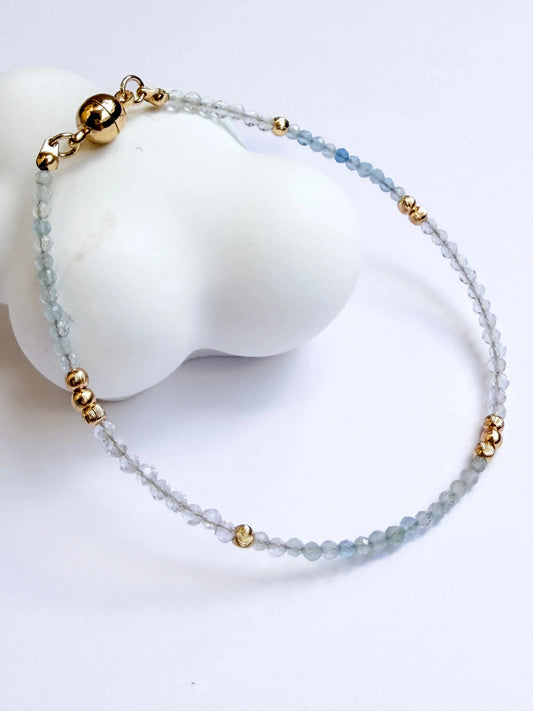 Japanese Minimalist Bracelet with blue aquamarine, clear crystal, and gold accents on a white surface