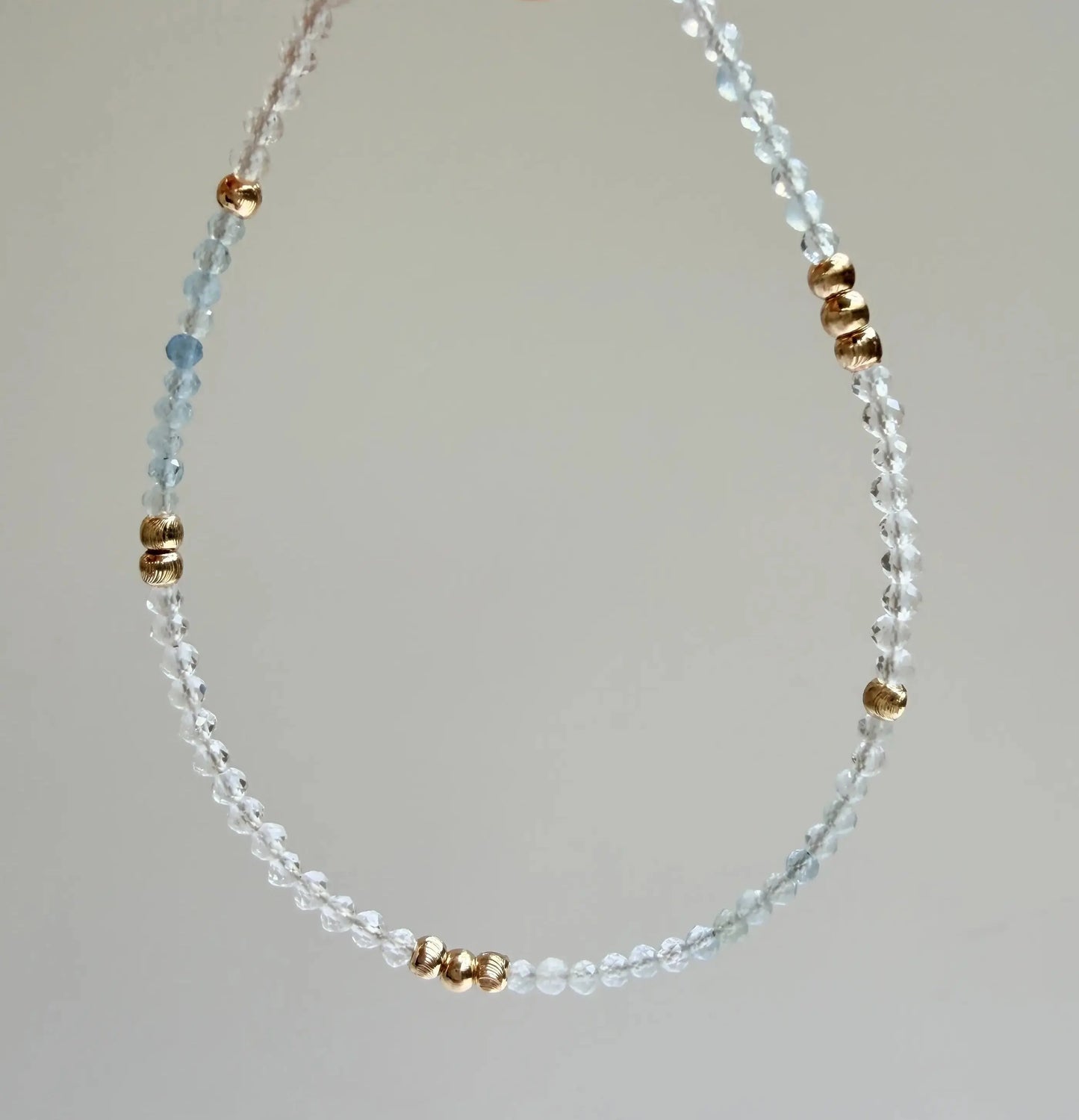 Japanese Minimalist Bracelet with blue aquamarine, clear crystal, and gold accents with a gray background