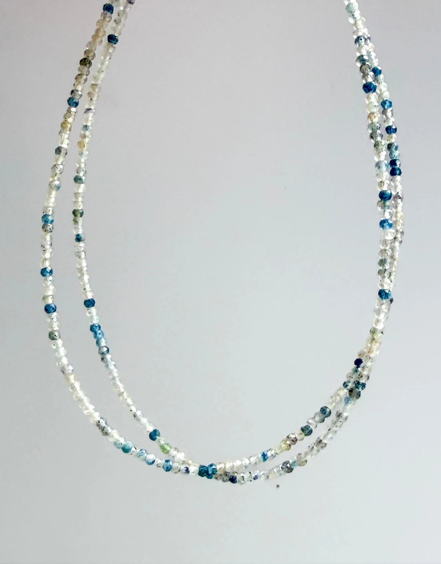 K2 Mineral with blue and gray multistrand beaded necklace on a gray background