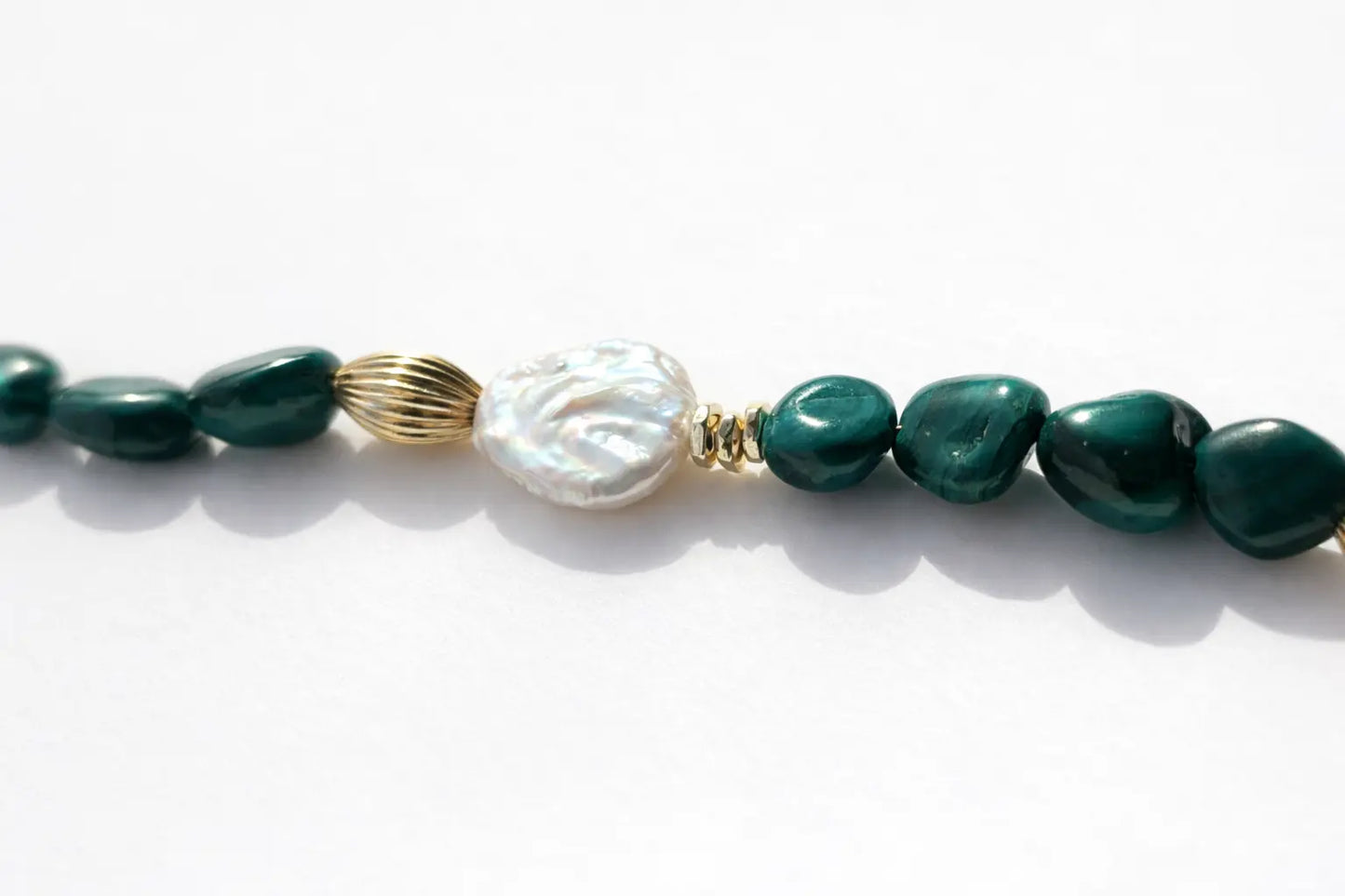 Necklace with green beads and a baroque pearl on a white background