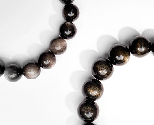silver sheen obsidian bracelet and gold sheen obsidian bracelet on white desk