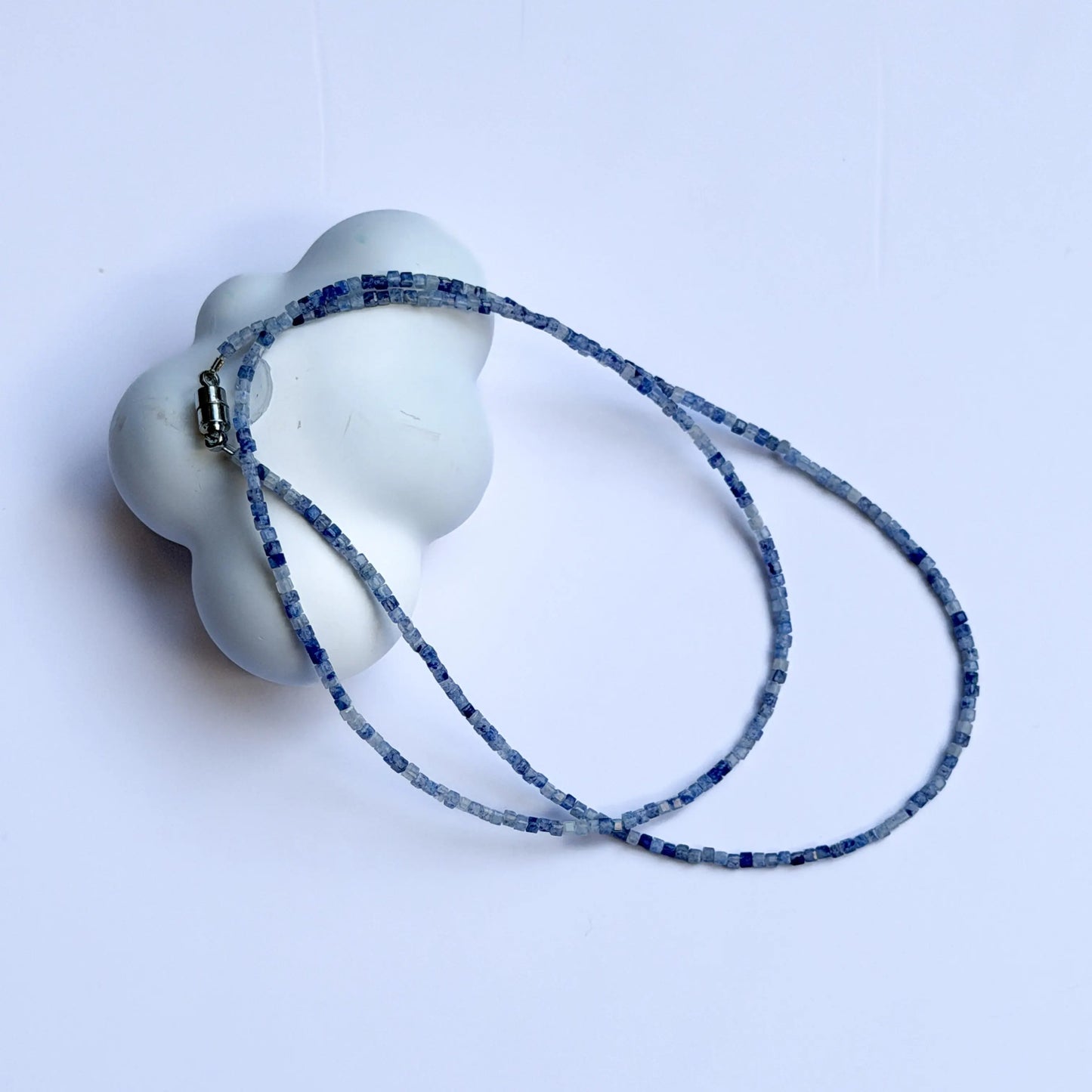 White ceramic object with a blue patterned sodalite crystal necklace on a light gray background