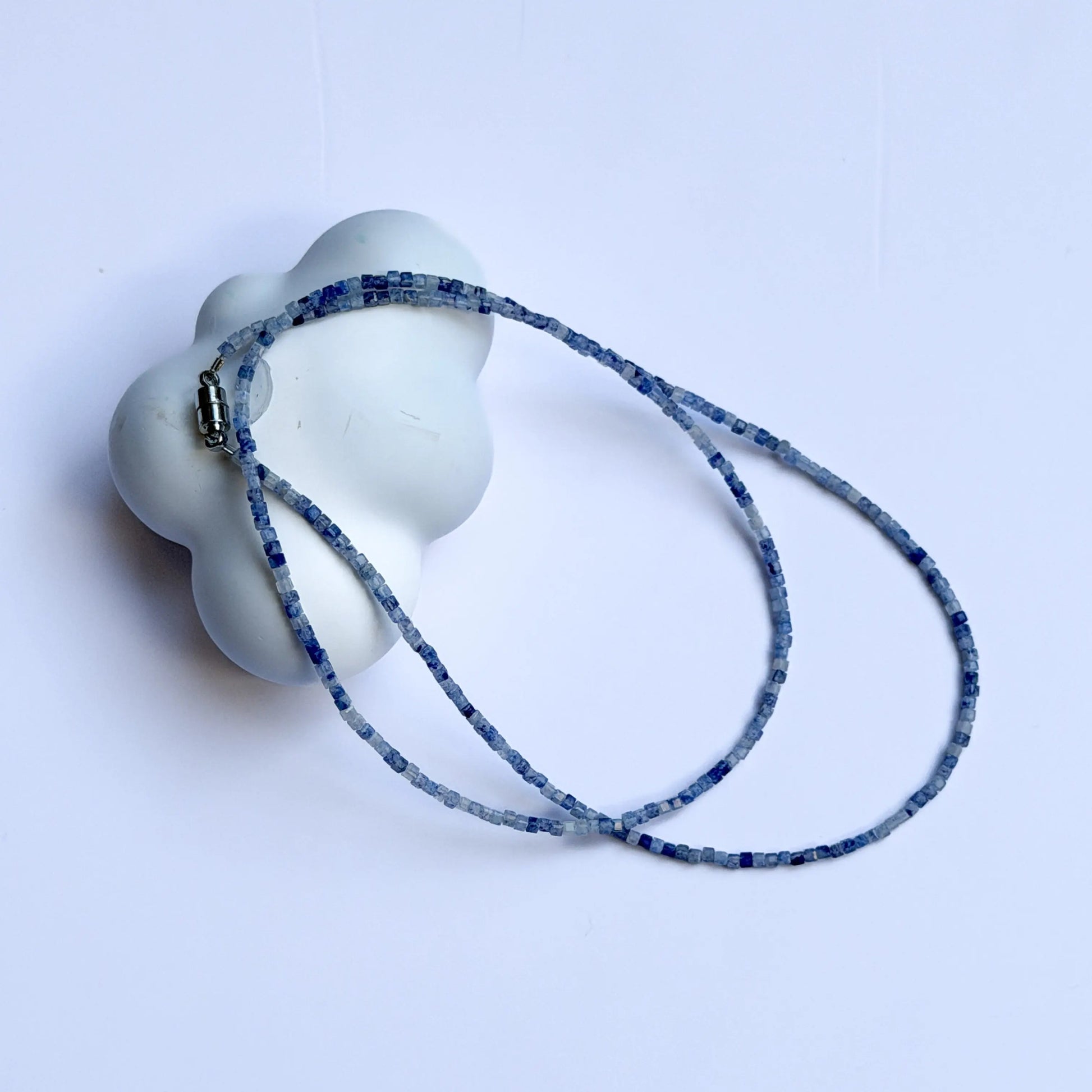 White ceramic object with a blue patterned sodalite crystal necklace on a light gray background