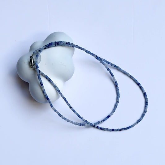 White ceramic object with a blue patterned sodalite crystal necklace on a light gray background