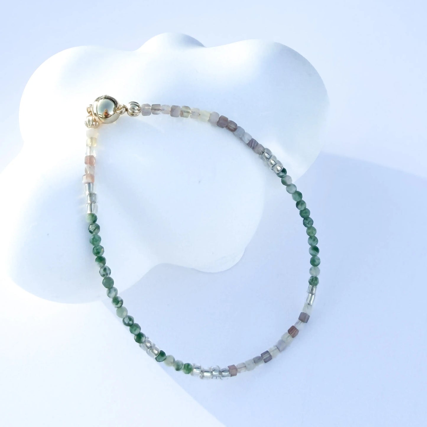 Bracelet with green and white jade beads on a white mannequin bust against a light blue background