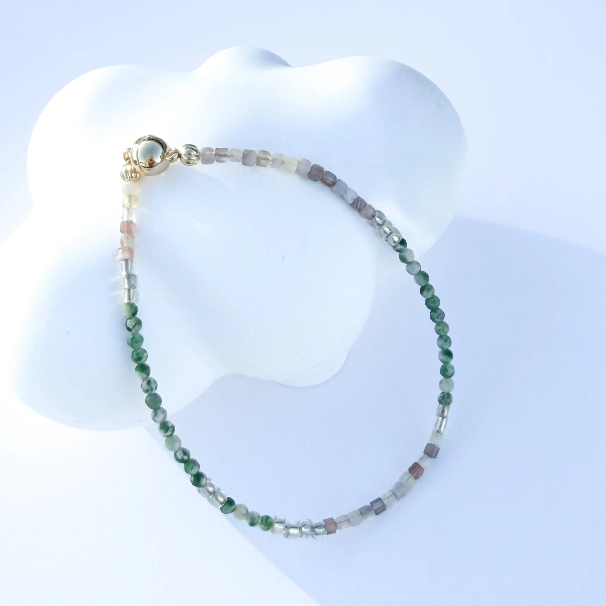 Bracelet with green and white jade beads on a white mannequin bust against a light blue background
